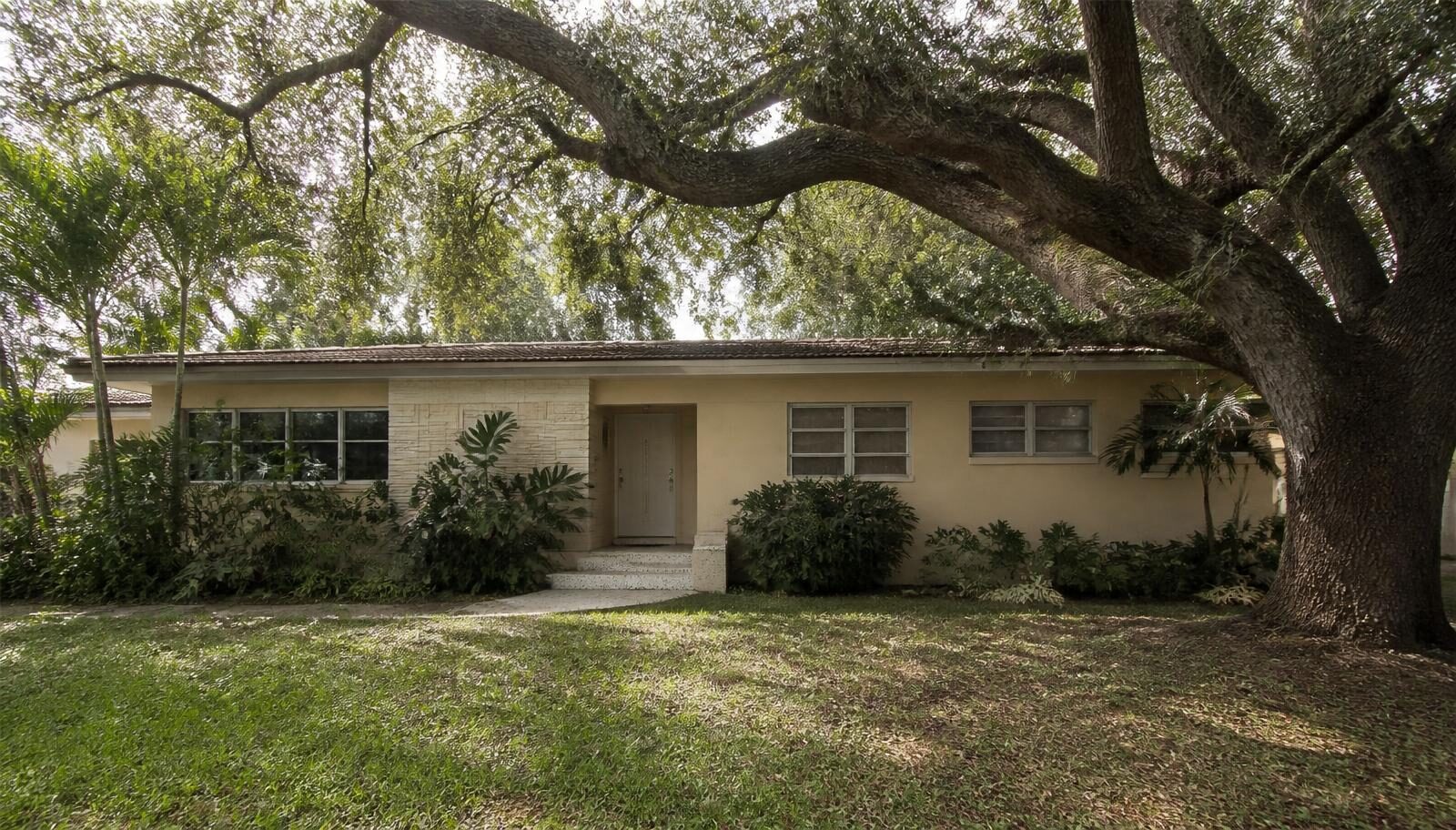 Older Miami residence with renovation potential shaded by mature oak trees